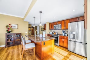 Une cuisine moderne dotée de meubles en bois, d’appareils électroménagers en acier inoxydable, d’un plan de travail en granit et d’un coin bar avec des tabourets.