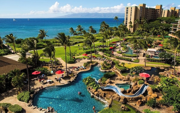 A resort with a swimming pool, a water slide, and a view of the ocean.