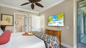 Une chambre d’hôtel avec un lit, un ventilateur de plafond, un téléviseur fixé au mur et une porte donnant sur une autre pièce.