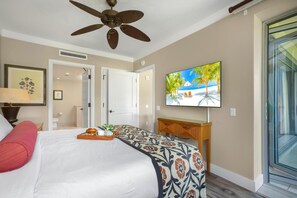 Ein Hotelzimmer mit einem Bett, einem Deckenventilator, einem an der Wand befestigten Fernseher und einer Tür zu einem weiteren Zimmer.