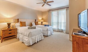 Ein Hotelzimmer mit zwei Betten, einem Deckenventilator, einem Fernseher und einem Nachttisch aus Holz mit einer Lampe.