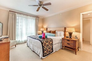 A hotel room with a bed, bedside lamps, a desk, a television, and a ceiling fan.