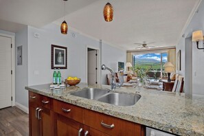 A kitchen with granite countertops, stainless steel sinks, wooden cabinets, and pendant lighting.