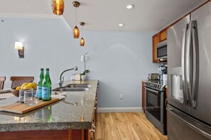 Eine Küche mit Granit Arbeitsplatte, Edelstahlgeräten, einem Holzespeisetisch und hängenden Pendelleuchten.