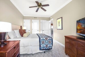 A hotel room with a bed, a ceiling fan, a TV, and a wooden dresser.