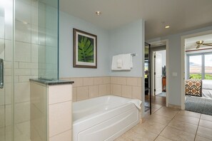 A modern bathroom with a bathtub, a glass shower enclosure, and a framed plant on the wall.