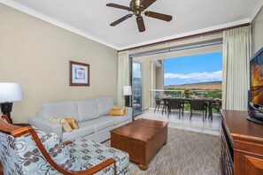 A hotel room with a sofa, coffee table, and a balcony with a table and chairs.