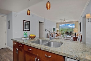 A kitchen with granite countertops, stainless steel sinks, wooden cabinets, and pendant lighting.