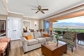 A spacious living room with a sofa, armchair, and coffee table, a balcony with a view of the landscape, and a ceiling fan. - Honua Kai | Ocean View 3 BR, Sleeps 10 | Car Incl. w/ 6+ Nights | HKK ML-1439 by KBM (Lahaina)