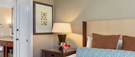 Quarto de hotel com uma cama, uma mesa de cabeceira com abajur, um quadro emoldurado e uma porta para o banheiro.