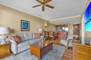 A living room with a sofa, coffee table, and TV, a kitchen with a microwave, and a dining area with chairs.
