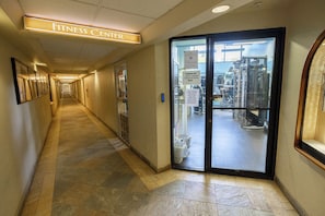 En gang der fører til et fitnesscenter, med et skilt over døren, en glasdør og et flisegulv.