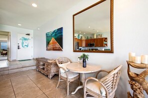 Un comedor con una mesa redonda, sillas de mimbre, un espejo grande y obras de arte en la pared.