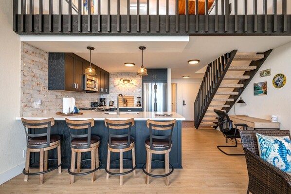 Una cocina moderna con una isla central, taburetes de bar y una escalera que lleva a un nivel superior.