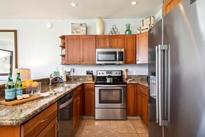 Una cocina moderna con armarios de madera, electrodomésticos de acero inoxidable, encimeras de granito y suelo de baldosas.