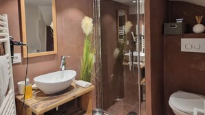 Un baño moderno con un lavamanos grande de color blanco, un espejo, una ducha con mampara de vidrio y un inodoro.