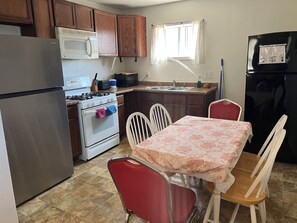 A kitchen with wooden cabinets, a stainless steel refrigerator, a microwave, a stove, a sink, and a dining table with chairs.