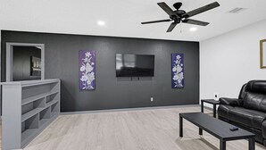 Una sala de estar moderna con un televisor de pantalla plana, un ventilador de techo y un sofá de cuero.