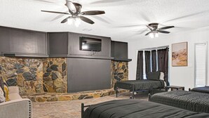 Una habitación con pared de piedra, dos camas, un televisor y ventiladores de techo.