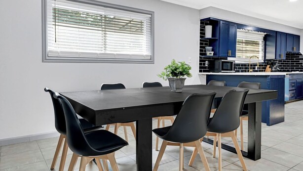 Una cocina moderna con armarios azul oscuro, una encimera negra y un comedor con mesa y sillas negras.
