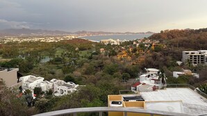 A coastal cityscape with a view of the sea, a park with palm trees, and residential buildings. - Unwind at this peaceful oasis. 3 minute drive to the beach (Manzanillo)