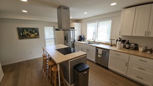 A modern kitchen with a central island, wooden stools, a stainless steel refrigerator, and a dishwasher. - New Renovation: 5BR Lake Delavan Retreat, Fire Pit, Huge Yard, Lake Access (Delavan)