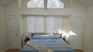 A bedroom with a large bed, two bedside tables with lamps, a window with blinds, and a door. - New Renovation: 5BR Lake Delavan Retreat, Fire Pit, Huge Yard, Lake Access (Delavan)