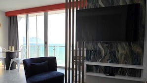 A modern living room with a large TV, a dark blue armchair, and a view of the ocean through large windows. - Ocean Pearl -  iconic views of Table Mountain & Robben Island. (Cape Town)