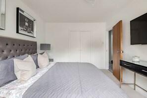 A bedroom with a large bed, a wardrobe, a television, and a framed picture on the wall.