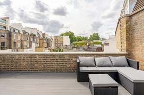 Una terraza en la azotea con zona de estar, paredes de ladrillo y vistas de los edificios circundantes.