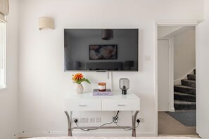A modern living room with a flat-screen TV mounted on a white console, a vase with flowers, a book, and a lamp. - The Hyde Park Townhouse (London)