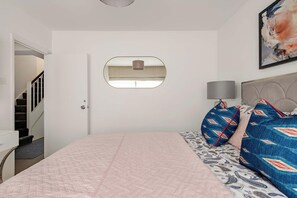 Un dormitorio con cama, lámpara de noche, espejo y una escalera que conduce a otra habitación.