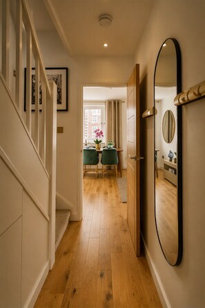 A hallway with wooden flooring, a staircase, a dining area with two chairs and a table, and a large mirror on the wall. - The Marylebone Signature Retreat (London)