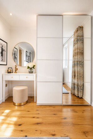 A room with a wooden floor, a white desk with a round mirror, a small stool, and a sliding door with a floral curtain. - The Marylebone Signature Retreat (London)