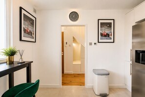 A modern kitchen with a stainless steel refrigerator, a trash bin, and framed pictures on the walls.