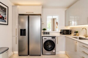 A modern kitchen with stainless steel appliances, a built-in washing machine, and a window with curtains. - The Marylebone Signature Retreat (London)