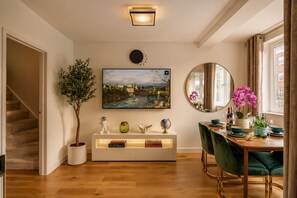 A dining area with a wooden floor, a round mirror, a painting, and a potted plant.