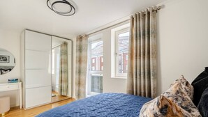Ein Schlafzimmer mit einem großen Bett, einem Kleiderschrank, einem Spiegel und einem Fenster mit Vorhängen.