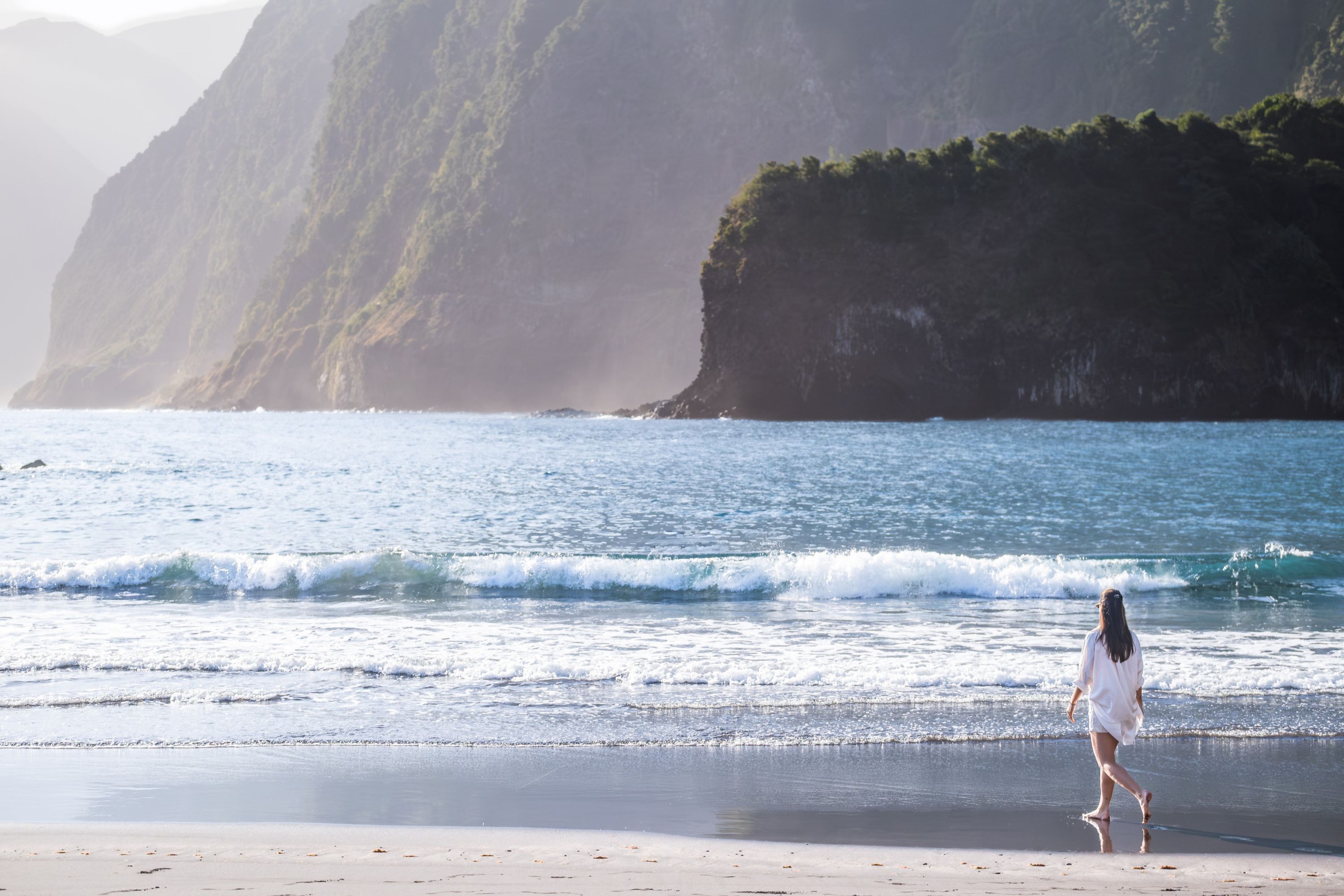 A beach with waves and a person walking on the sand.
