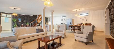 A spacious living area with a sofa, armchairs, a coffee table, and pendant lights. A staircase leads to an upper level.
