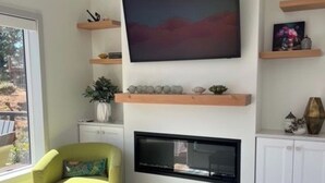 Una sala de estar moderna con un televisor de pantalla plana grande montado en la pared, un sillón verde, una pequeña mesa de centro con un adorno, y una chimenea debajo del televisor.