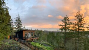 Una cabaña moderna con terraza, rodeada de bosque y montañas.