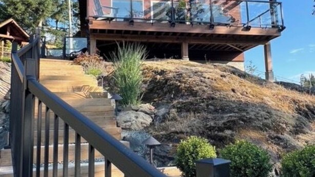Una casa moderna con terraza de madera y barandilla de cristal que da a una ladera rocosa.