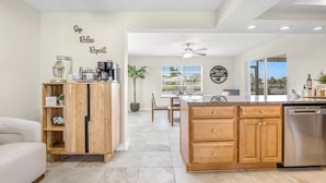 A modern kitchen with wooden cabinets, a built-in dishwasher, and a central island. There is a dining area with a table and chairs, and a ceiling fan above. - SCALLOP TIME AT WATERFRONT ESCAPE DIRECT GULF ACCESS, GOLF CART & KAYAKS. (Hernando Beach)