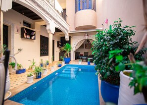 A pool area with a tiled floor, surrounded by potted plants and a seating area with a table and chairs. - Riad tala (Marrakech)