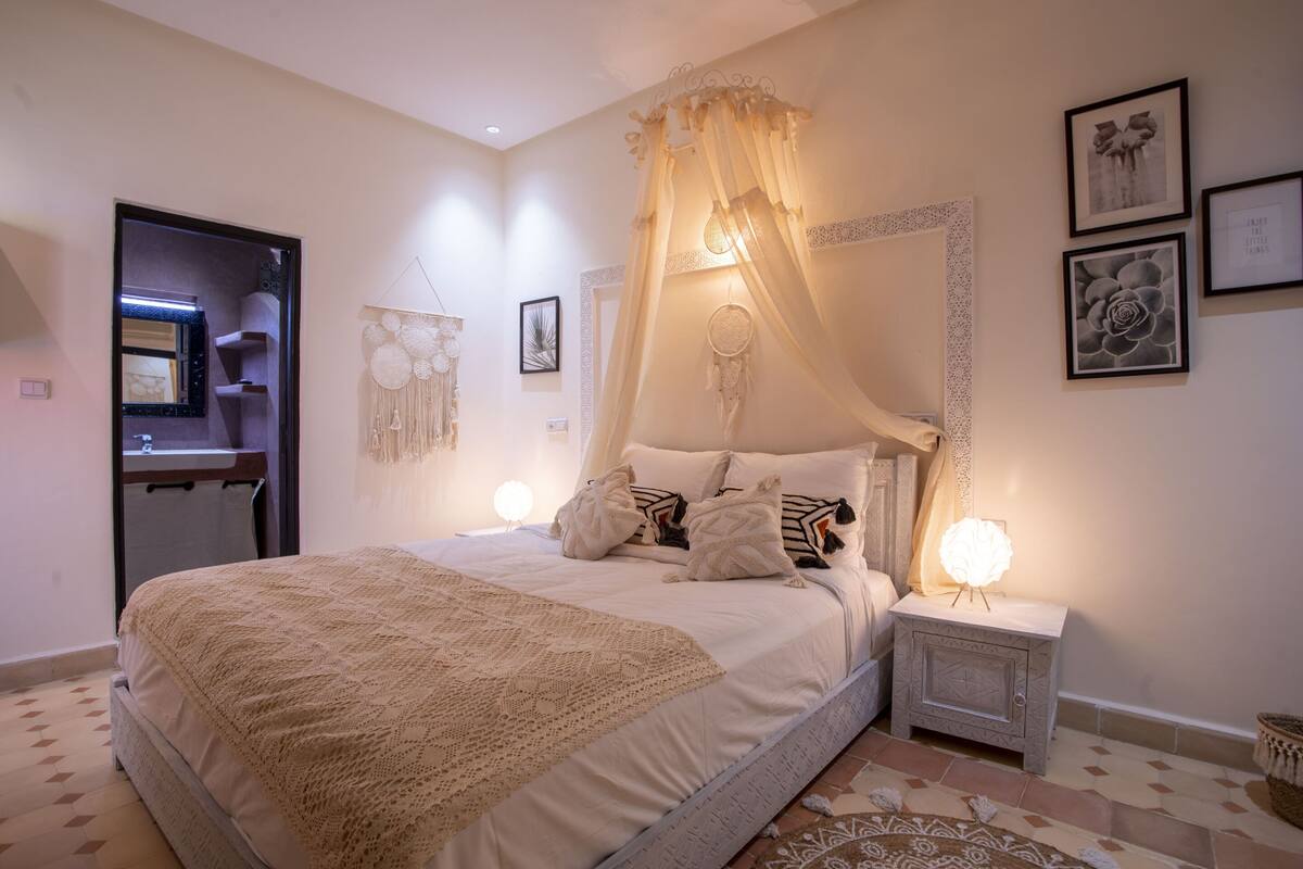 A bedroom with a four-poster bed, bedside lamps, and wall art.