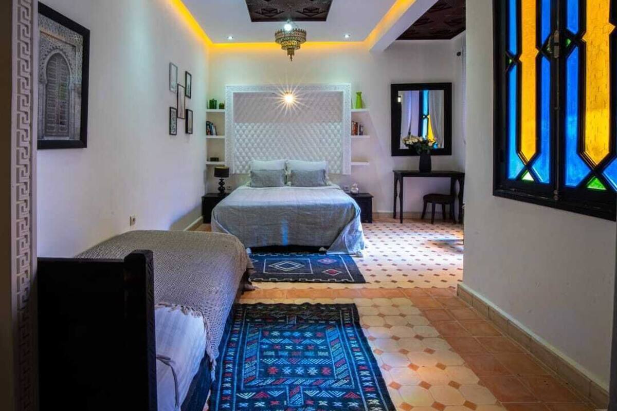 A bedroom with a bed, bedside tables, a nightstand, a dresser, a mirror, and a window with stained glass.