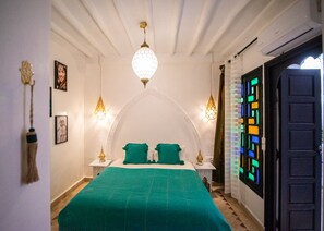 A room with a bed, two bedside tables, a hanging light fixture, and a door with colorful glass panels. - Riad tala (Marrakech)