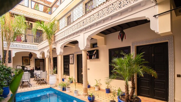 A courtyard with a swimming pool, potted plants, and a dining area. - Riad tala (Marrakech)