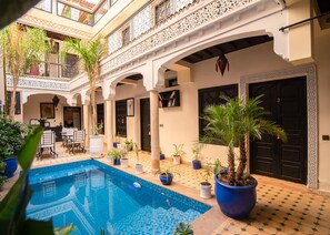 A courtyard with a swimming pool, potted plants, and a dining area. - Riad tala (Marrakech)